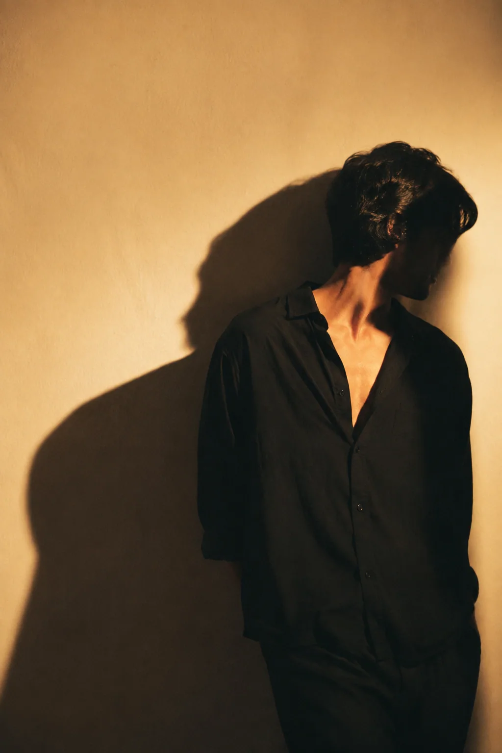 Anonyme Portraitstudie vor einer hellen Wand mit diagonalen Schatten